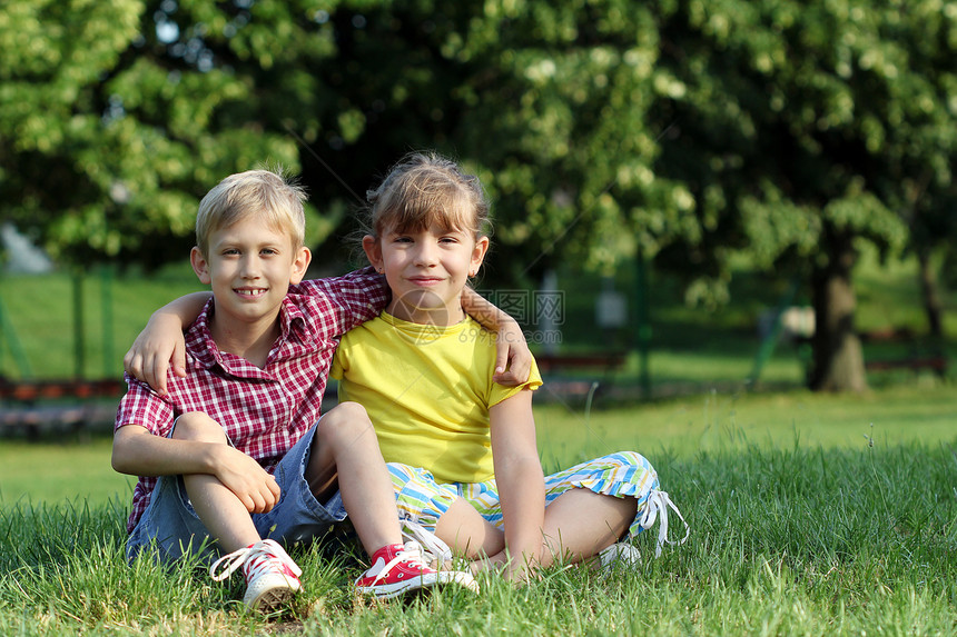 快乐的小女孩和男孩坐在草地上图片