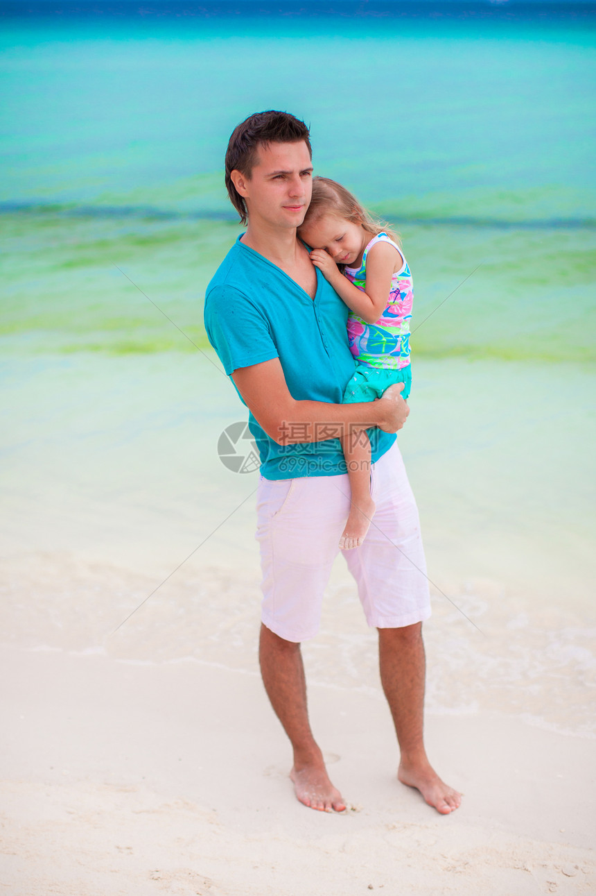 年轻爸爸和他的小女儿在热带白沙滩上走来走去图片