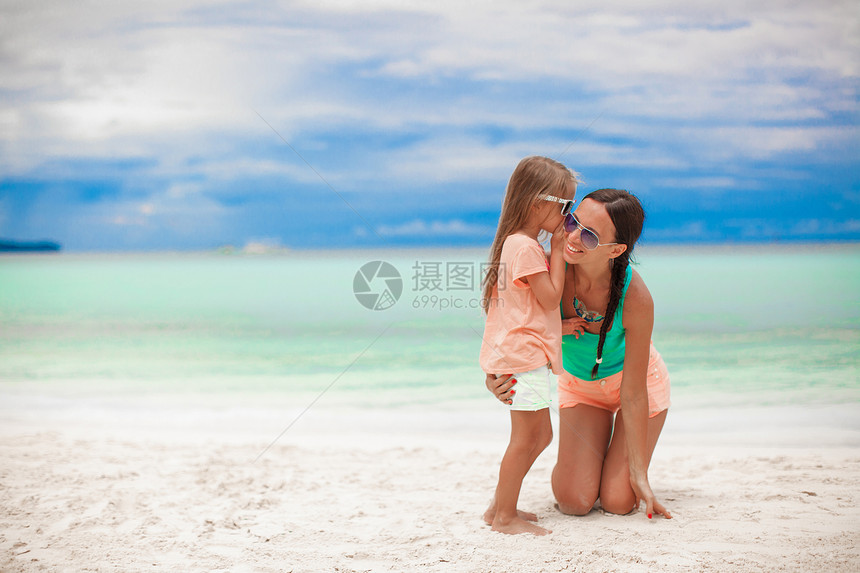 年轻母亲和她可爱的小女孩 在白沙滩上低语假期父母情调海滩妈妈太阳镜热带女儿婴儿耳语图片