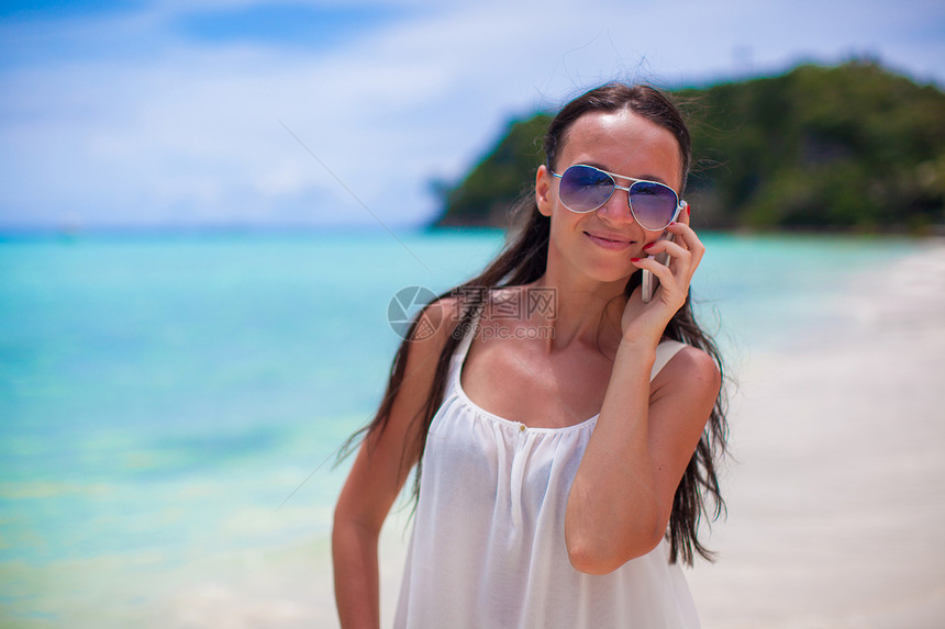海滩上的年轻美女 在电话上聊天的少女细胞幸福女孩漫游手机消息异国海洋情调女性图片