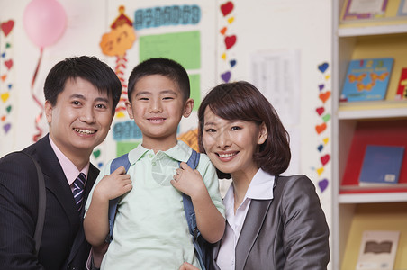 父母和儿子在教室上课商务背包团结男孩们母亲套装微笑衬衫摄影红发背景图片