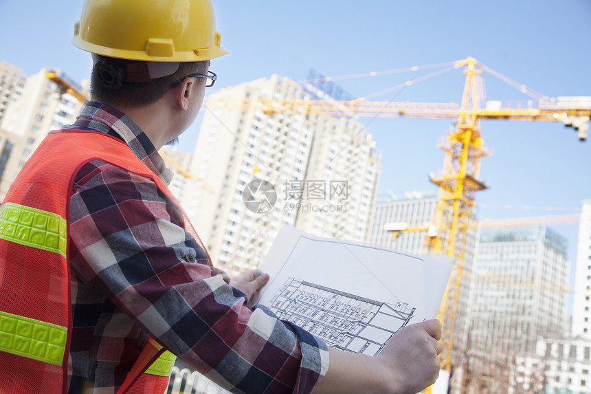 建筑设计师在建筑工地的户外建筑蓝图衬衫进步外观头饰眼镜胡须纽扣安全帽承包商起重机图片