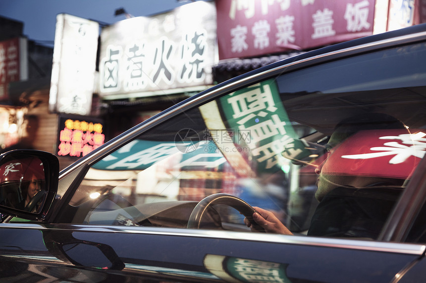 青年男子晚上开车穿过北京 在车窗上反射着路牌的发光店牌图片