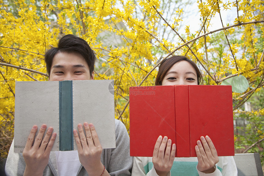 年轻快乐的情侣坐在一起阅读书本 面对部分障碍 在春季户外露天图片