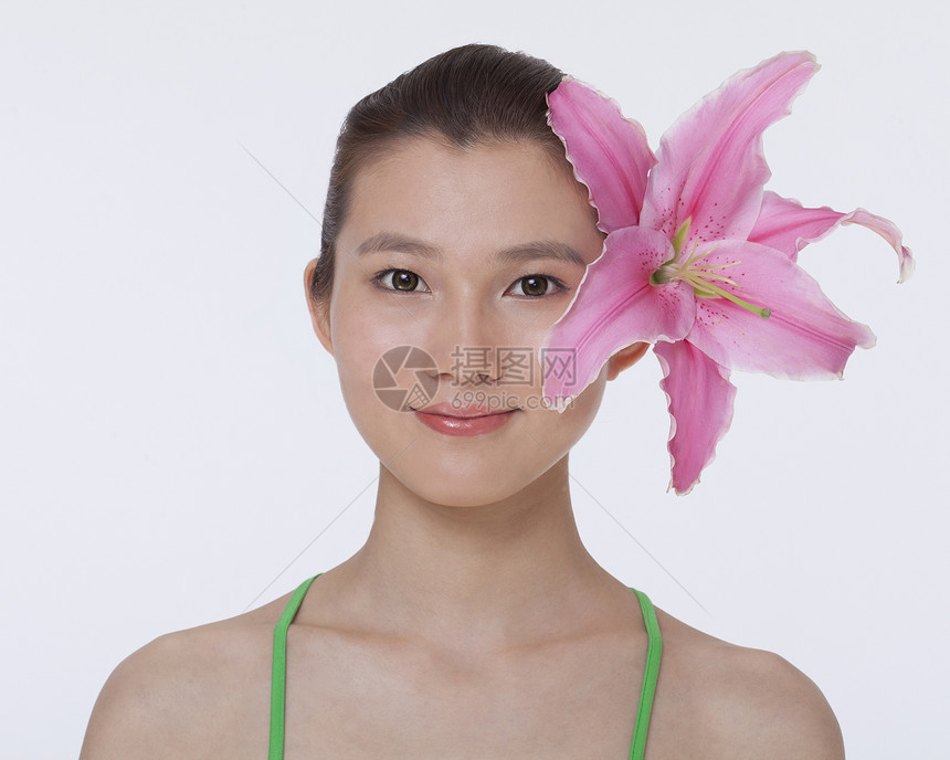 年轻 微笑 美丽的女人的肖像 带着一朵粉红色大花 藏在她耳后头发头肩影棚场景耳朵服装摄影对象背心绿色图片