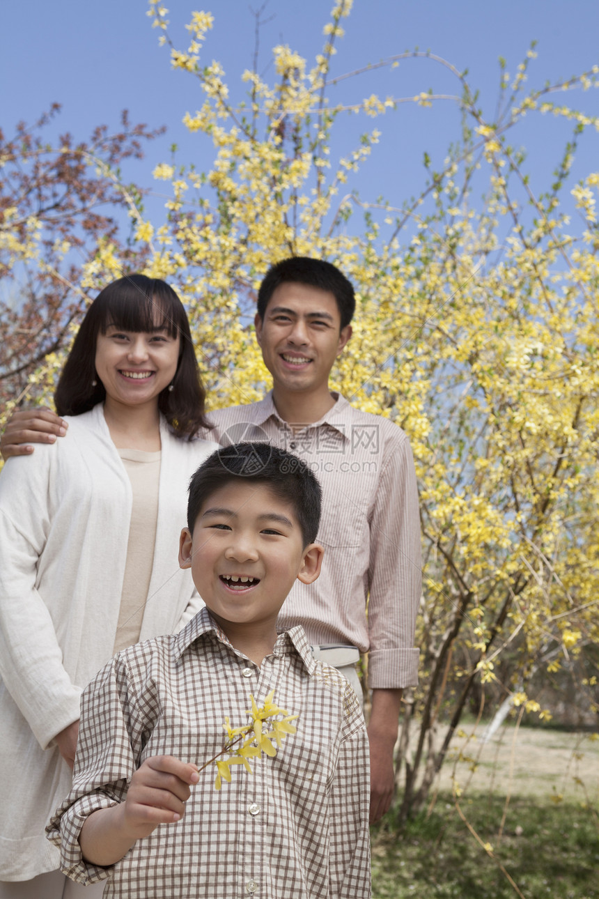 春天 在公园里拿着一朵黄色花朵的小孩和微笑的家人的肖像图片