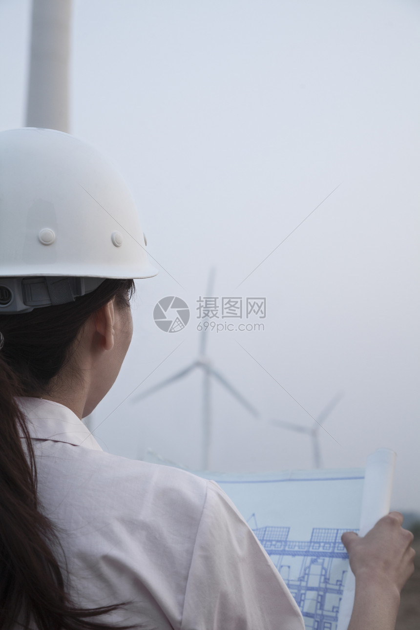 年轻女工程师在肩上看蓝图 前面有风力涡轮机的年轻女工程师图片