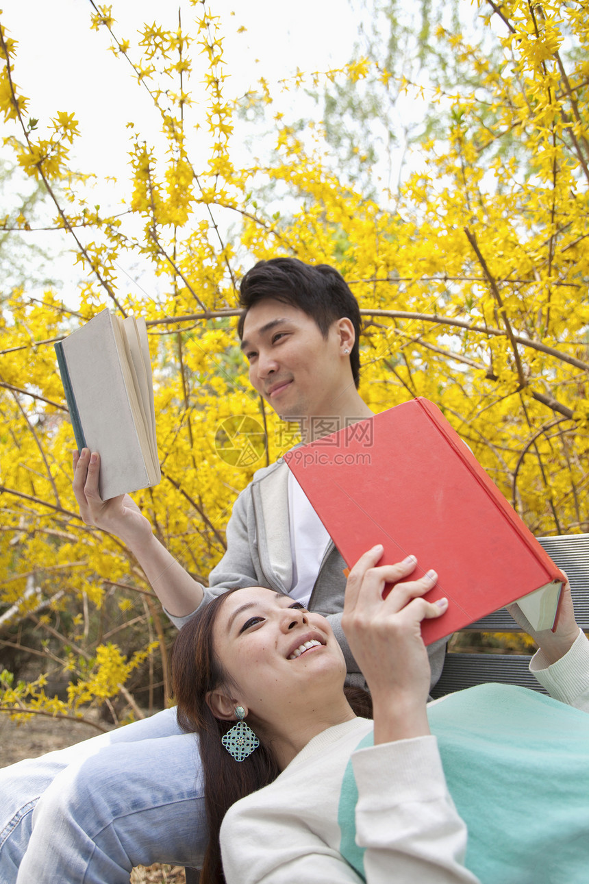 年轻快乐的夫妇躺在公园的长椅上 享受春天在户外读书的乐趣视图两个人服装年轻人男朋友活力幸福团结微笑摄影图片
