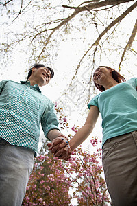 快乐笑笑的年轻夫妇 在春天在公园握手 低角度观背景图片