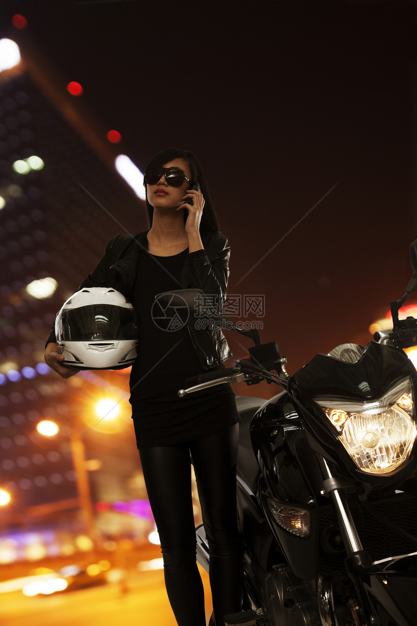 北京戴墨镜的年轻女子晚上打电话 站在摩托车旁图片