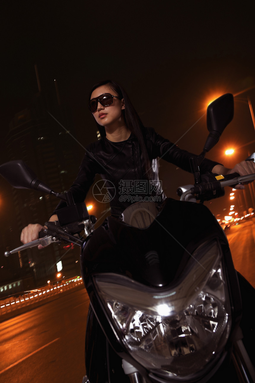 美丽的年轻女子晚上骑着摩托车 在太阳眼镜下穿过城市街道 在夜间穿梭皮革体力收腰运动太阳镜交通黑发倾斜活动长发图片