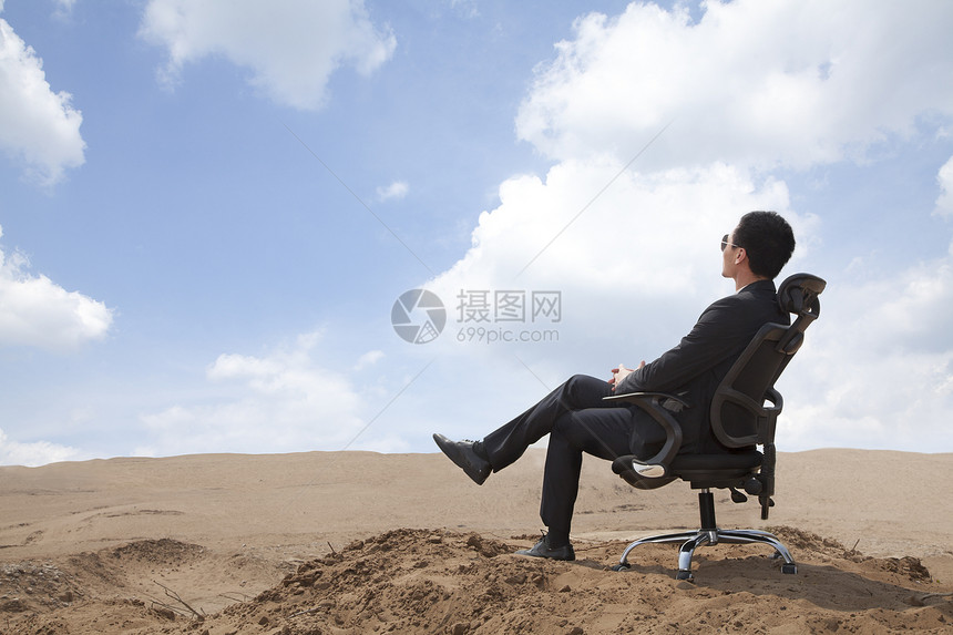 坐在沙漠中间的办公椅上的年轻商务人士图片