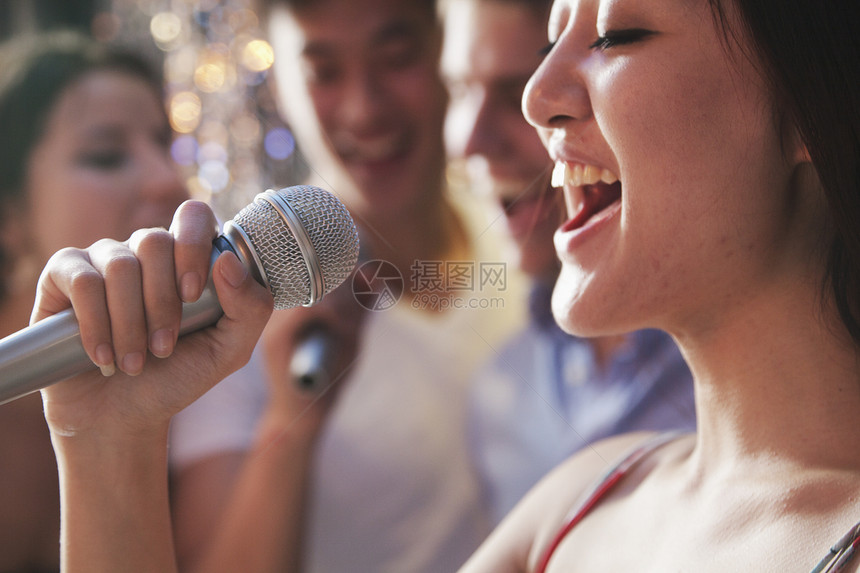紧贴近身的年轻女子拿着麦克风 在卡拉OK唱歌 朋友在背景中唱歌图片