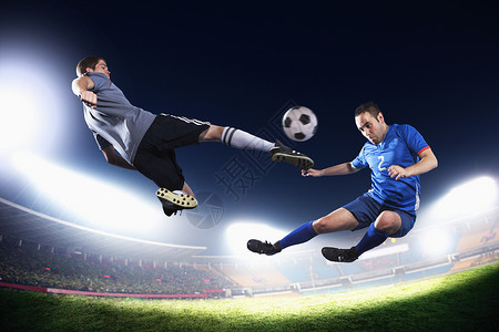 卫冕两个中空足球运动员踢足球球 晚上在体育场的灯光下打背景背景