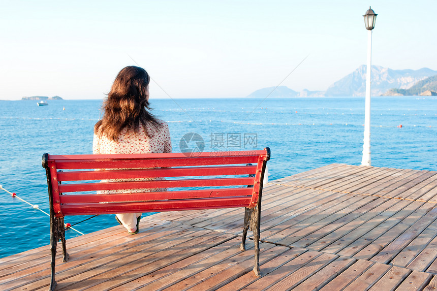 女孩坐在海边码头的长凳上 然后反射图片