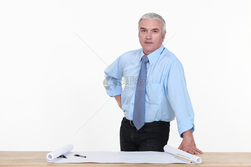 灰发建筑师站在工作桌旁图片