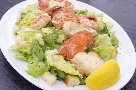 凯撒沙拉 与大虾鲑鱼和白鱼午餐蔬菜黑色盘子白色敷料食物起动机面包块餐厅背景