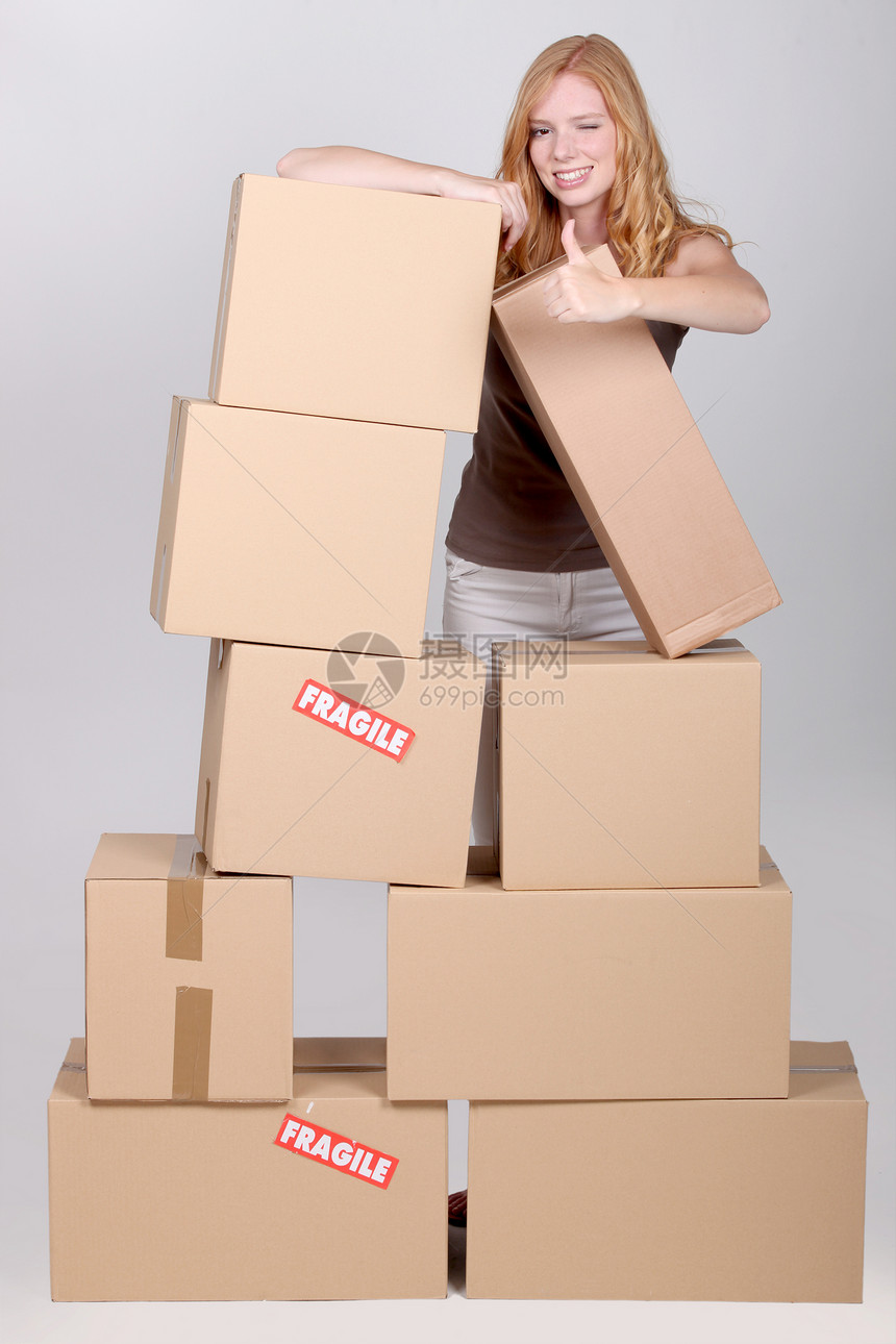 妇女站在一堆纸板箱旁红发房子盒子成人贮存牛仔裤棕色白色工作室倾斜图片