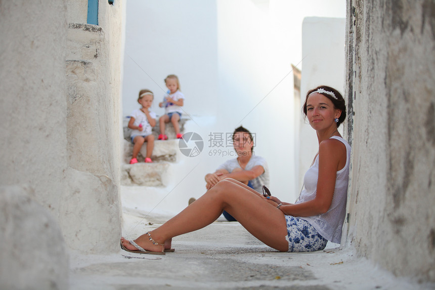 年幼母亲背景 她可爱的女儿和丈夫在塞克拉底群岛一个希腊村庄中的丈夫图片