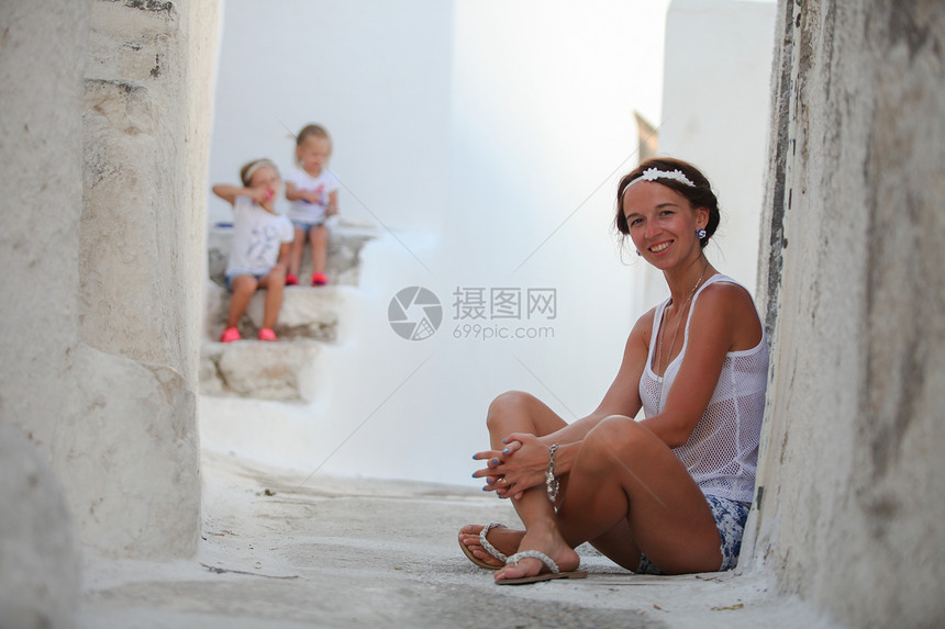 快乐的母亲在基克拉迪群岛的一个希腊村庄里给她可爱的女儿们做背景图片