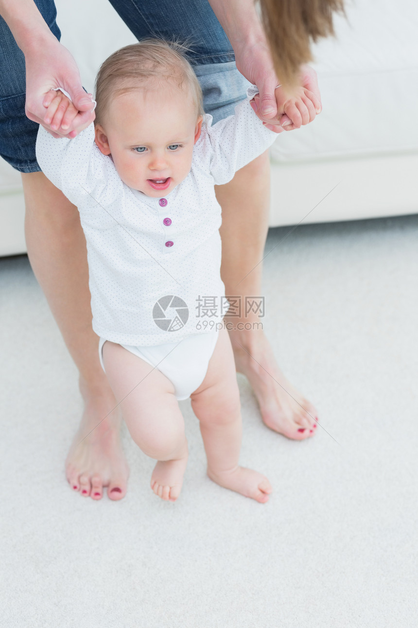 母亲帮助她的孩子走路赤脚沙发金发女郎公寓女孩浅色新生活房子短发双手图片