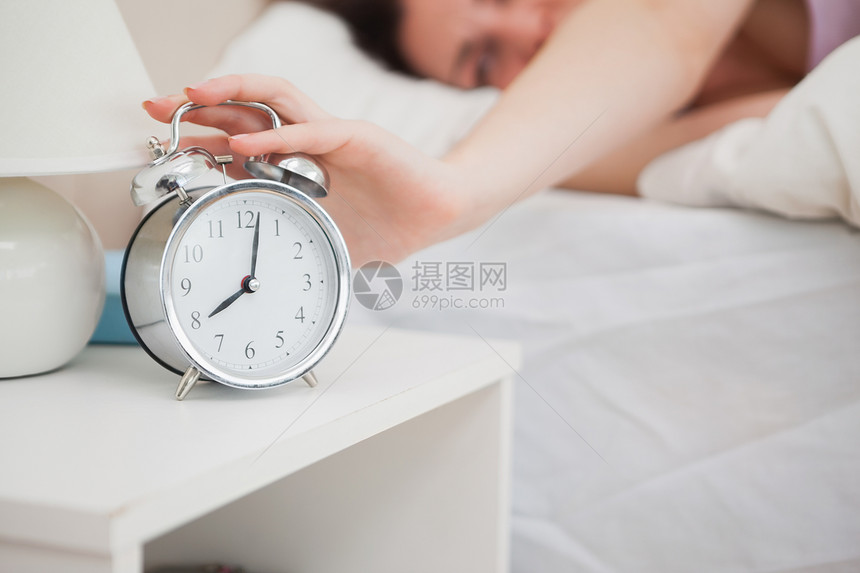 躺在床上的沉睡妇女将手伸向闹钟图片
