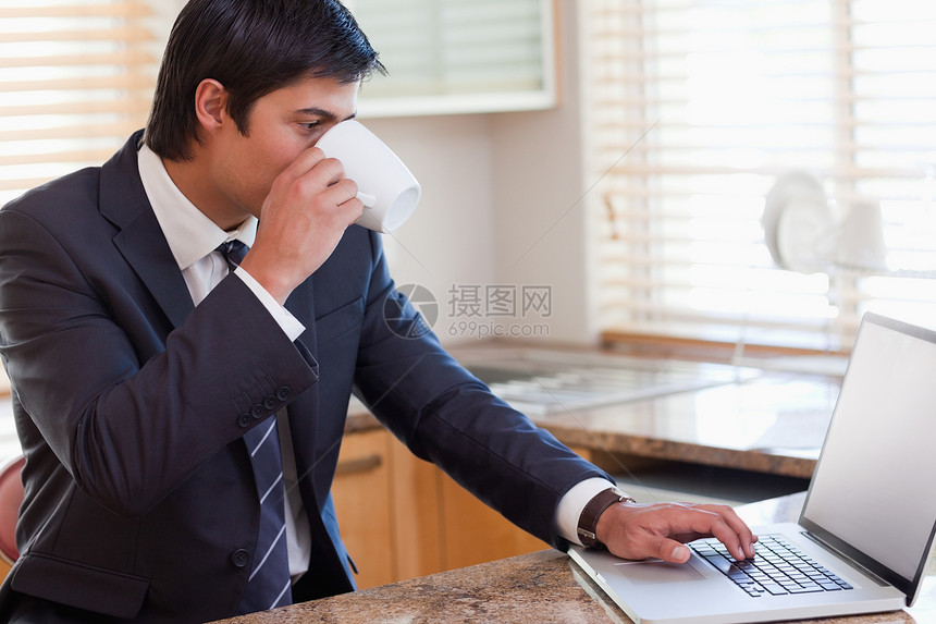 商务人士在喝咖啡时使用笔记本电脑男人咖啡杯厨房男性商务套装家庭生活技术房子台面图片
