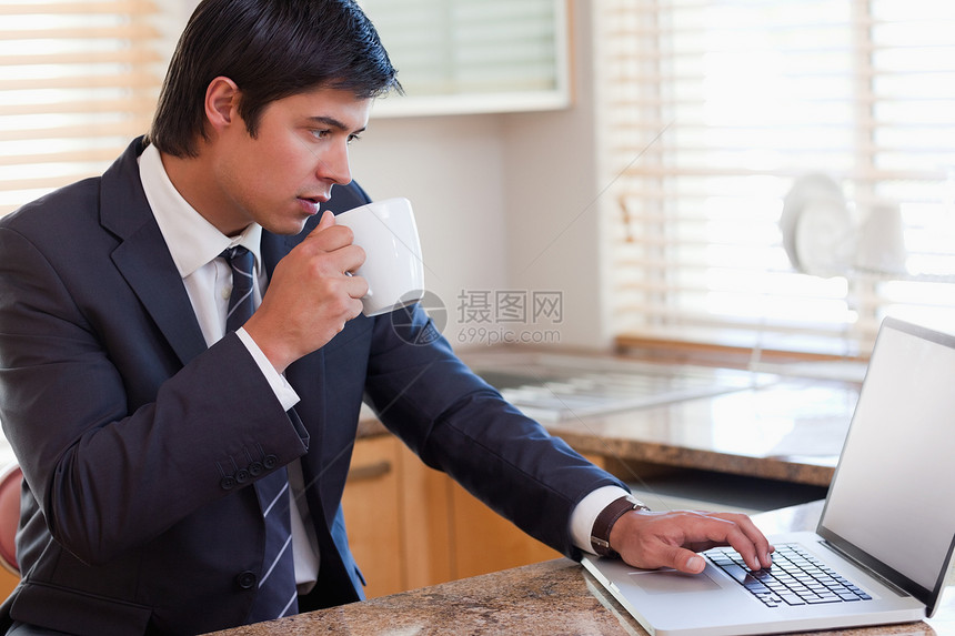 商务人士在喝咖啡时使用笔记本电脑男人专注技术商务房子台面套装厨房人士家庭生活图片