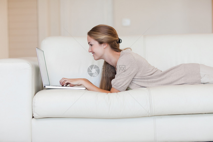 在沙发上使用笔记本电脑的临时妇女侧边视图幸福家庭生活客厅金发女性浅色长发说谎头发金发女郎图片