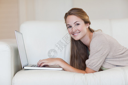 在沙发上使用笔记本电脑的说谎金发女郎浅色头发技术女性女士房子客厅闲暇背景图片