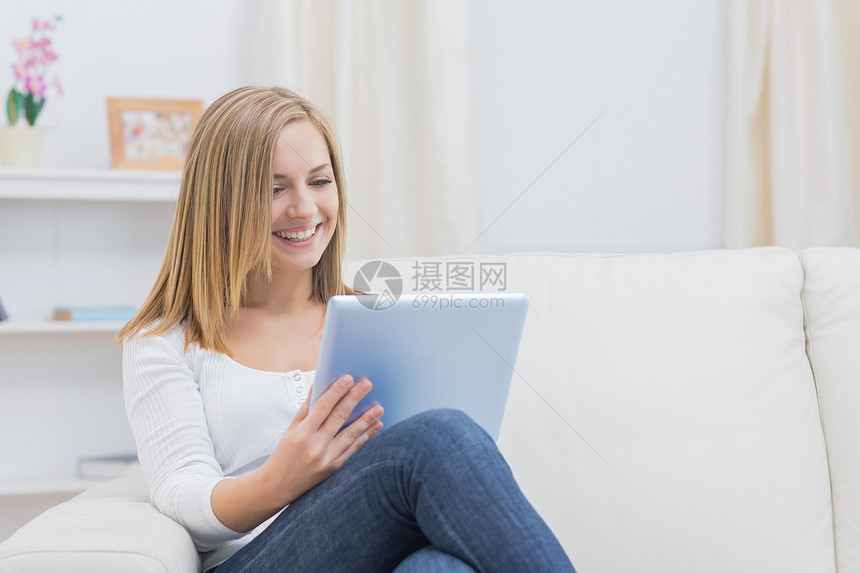 在沙发上使用数字平板纸的偶然快乐妇女女士电脑牛仔裤微笑客厅技术触摸屏金发女郎长椅幸福图片
