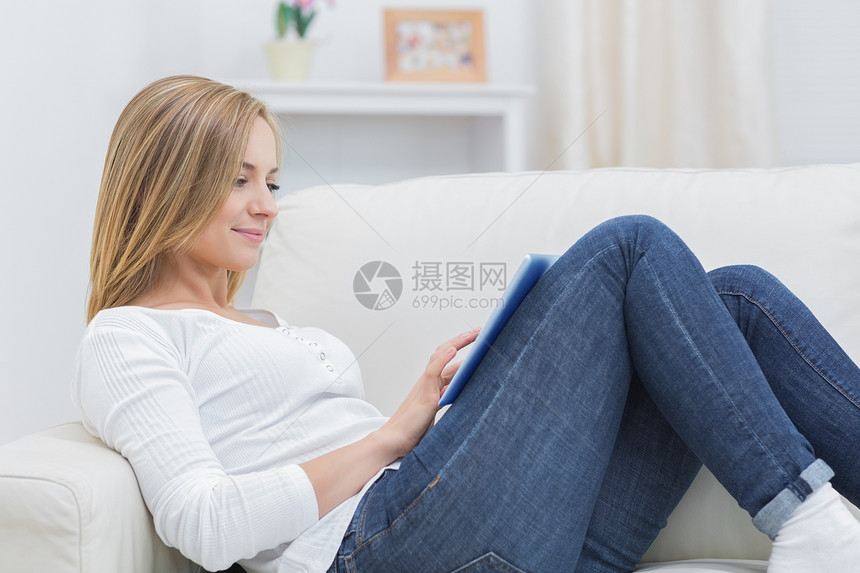 使用沙发上的数字片子的临时妇女侧边视图牛仔裤金发闲暇浅色客厅技术头发长椅电脑金发女郎图片