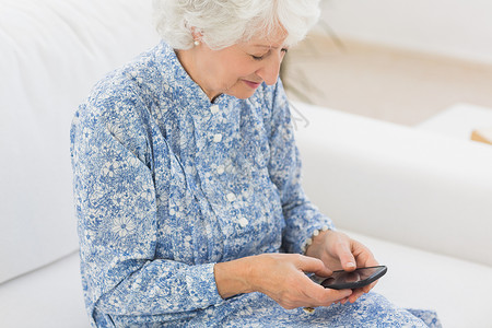 使用智能手机的年长快乐妇女屏幕女士微笑退休客厅岁月头发技术流金白色背景图片