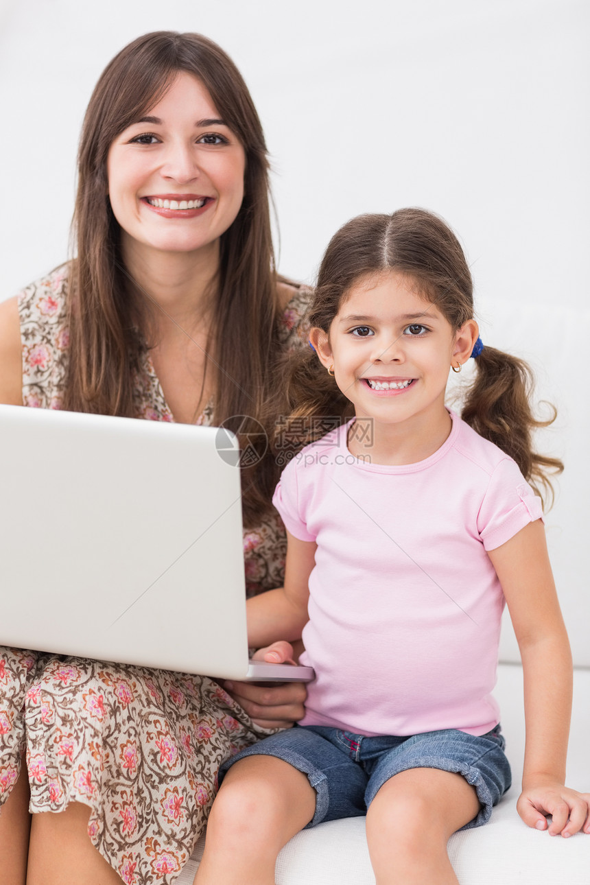 母亲和女儿用笔记本电脑微笑沙发快乐女孩头发棕色技术长椅女士家庭女性图片