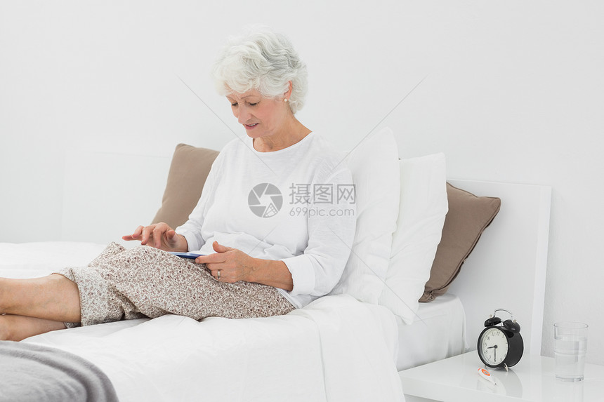 使用数字平板电脑的老年妇女枕头退休家庭白色闹钟岁月女性女士桌子触摸屏图片