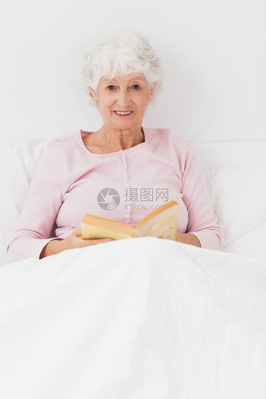 微笑的女人在床上看书小说卧室闲暇枕头住所房子坐垫公寓家庭女士图片