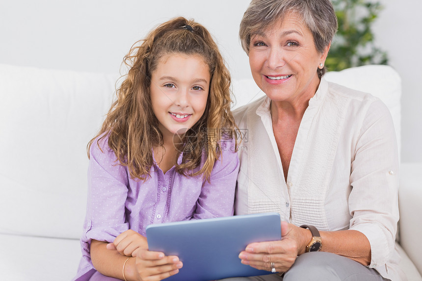 小女孩和祖母用平板电脑看照相机 看着镜头图片