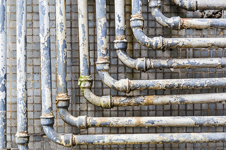 墙上一系列平行的旧管线线条金属关节基础设施建筑对角线管道导管间距灰色背景