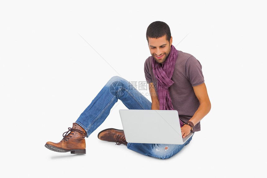 使用笔记本电脑坐在地板上时戴着围巾的微笑者图片