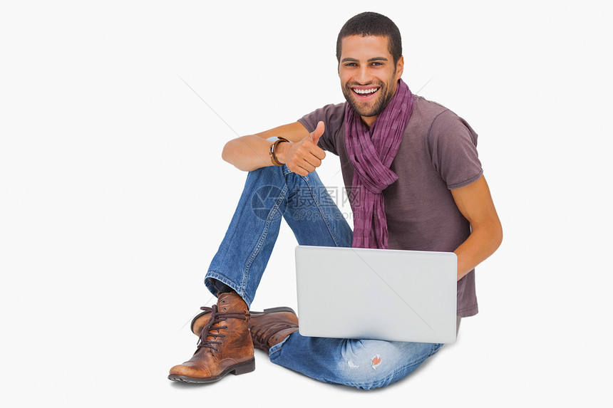 快乐的人坐在地板上 用笔记本电脑给人拇指图片