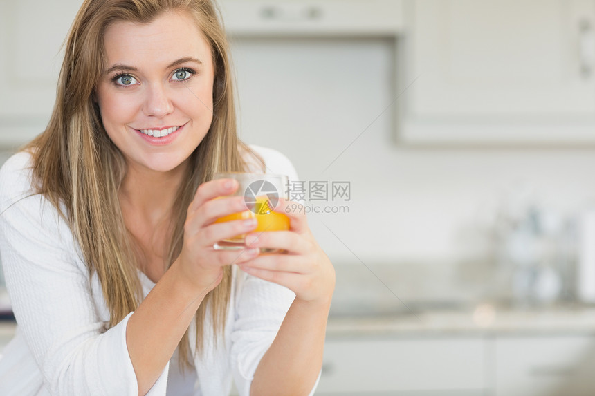 女人拿着橙汁玻璃浅色台面头发快乐金发房子睡衣家庭女性图片
