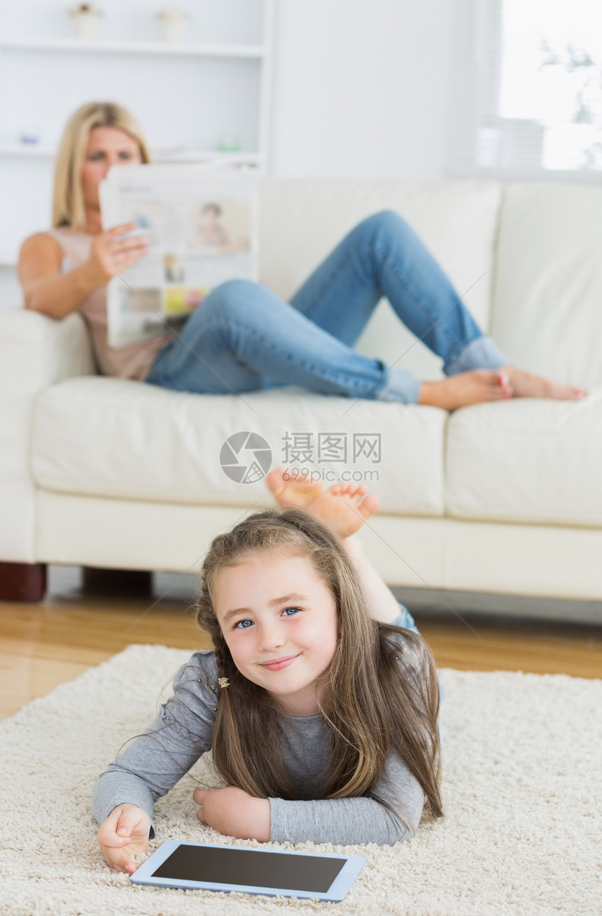 微笑的小女孩使用平板电脑 而她的母亲正在看报纸图片