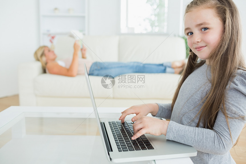 在笔记本电脑上工作的女孩和母亲看报纸图片
