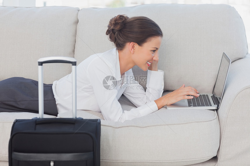 商业妇女用笔记本电脑和手提箱躺在沙发上图片