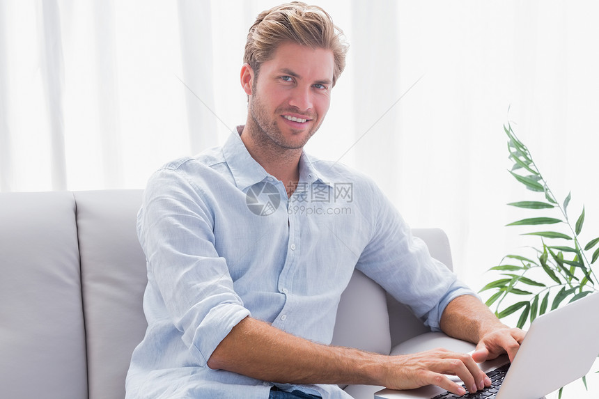 男人用笔记本电脑坐在沙发上休息室房子公寓头发微笑技术客厅男性长椅浅色图片