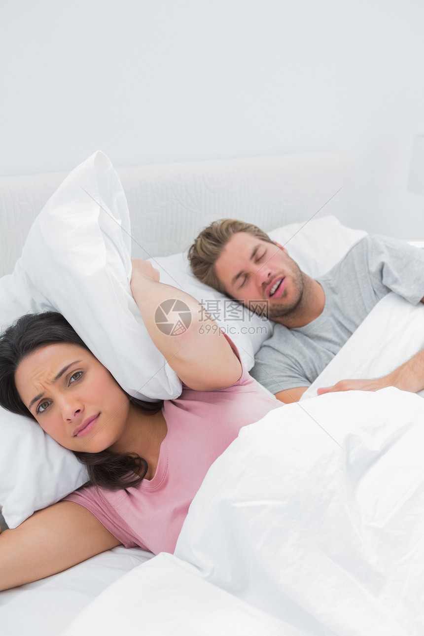 女人在丈夫打呼噜旁边用枕头遮住耳朵 紧挨丈夫打呼噜图片
