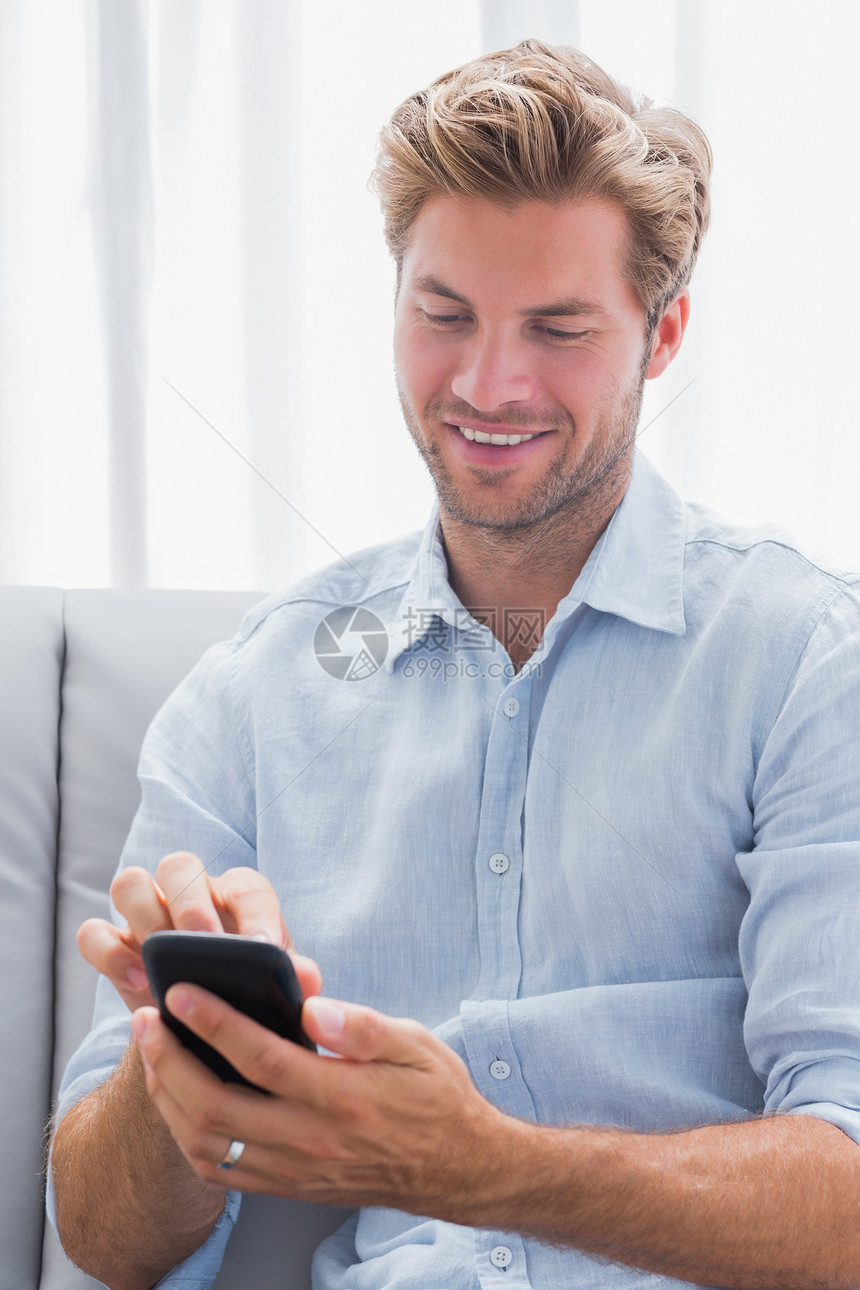 在沙发上使用智能手机的 快乐的男人图片