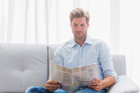 男人在沙发上看报纸公寓闲暇男性快乐阅读休息室浅色头发金发短发背景图片