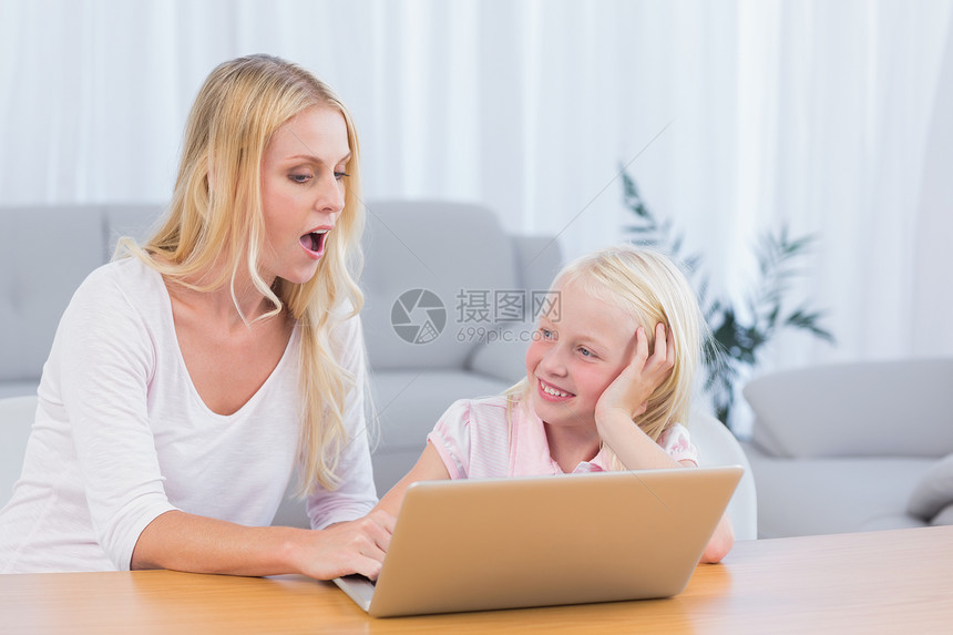 母亲和女儿使用手提笔记本电脑女士金发金发女郎浅色互动技术长发客厅家庭桌子图片
