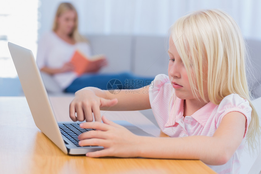 小女孩使用笔记本电脑 而她的母亲却在Couc上阅读图片